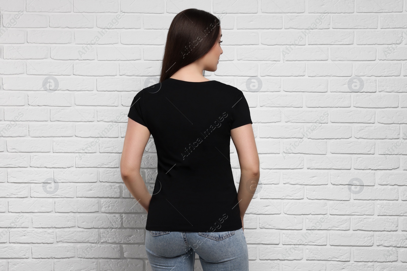 Photo of Woman wearing stylish black T-shirt near white brick wall, back view