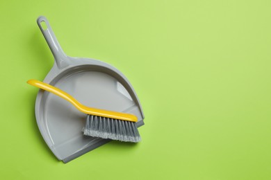 Photo of Plastic hand broom and dustpan on light green background, top view. Space for text