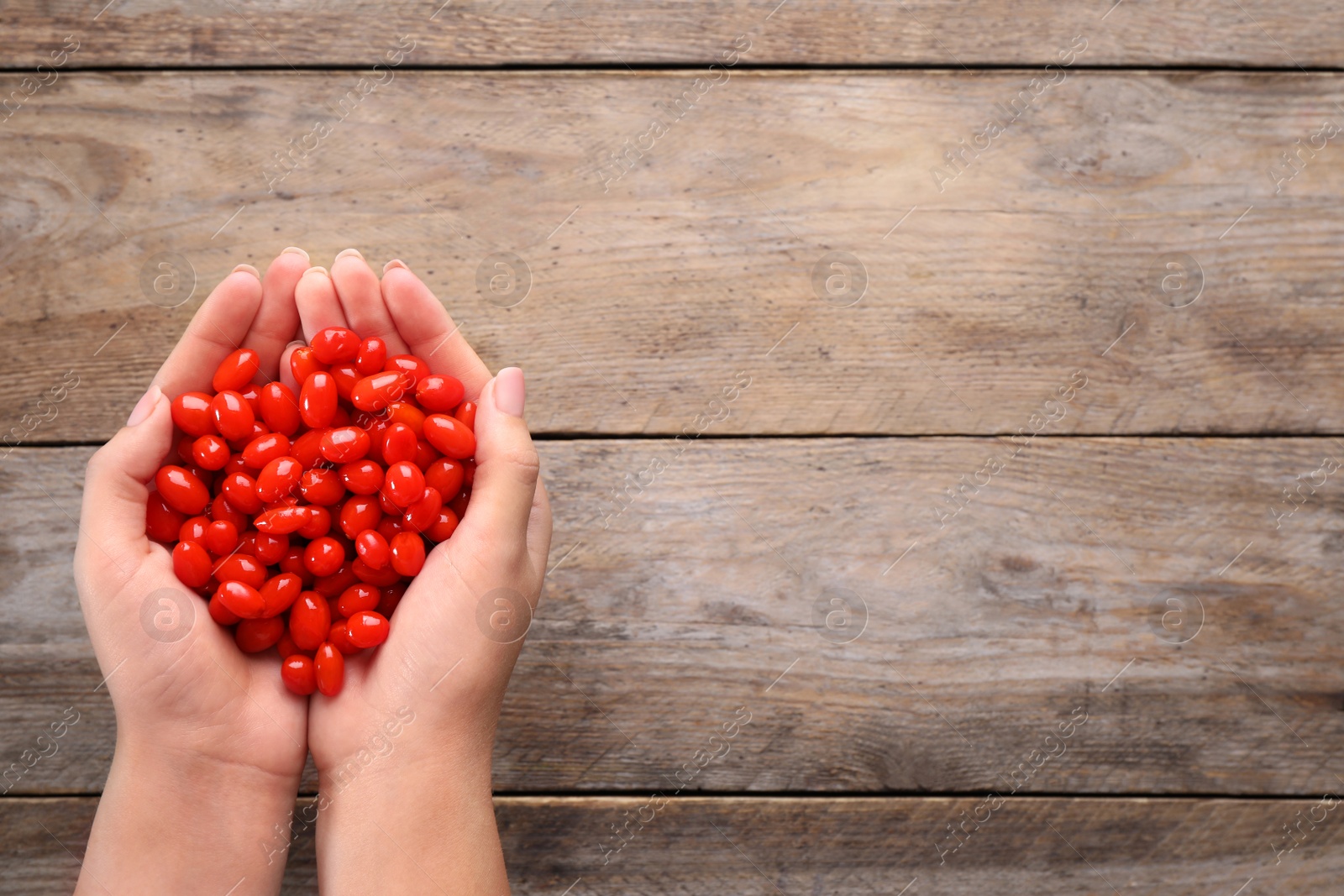 Photo of Woman holding fresh goji berries on wooden background, top view. Space for text