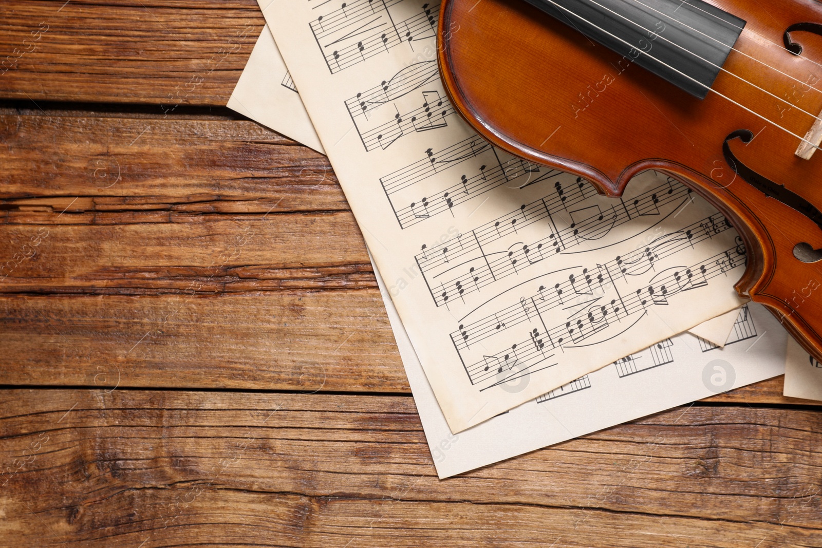 Photo of Violin and music sheets on wooden table, top view. Space for text