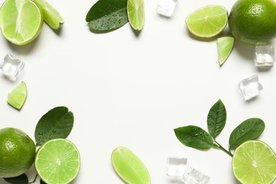 Frame made of ripe limes with green leaves and ice cubes on white background, flat lay