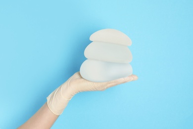 Photo of Doctor holding silicone implants for breast augmentation on color background, space for text. Cosmetic surgery