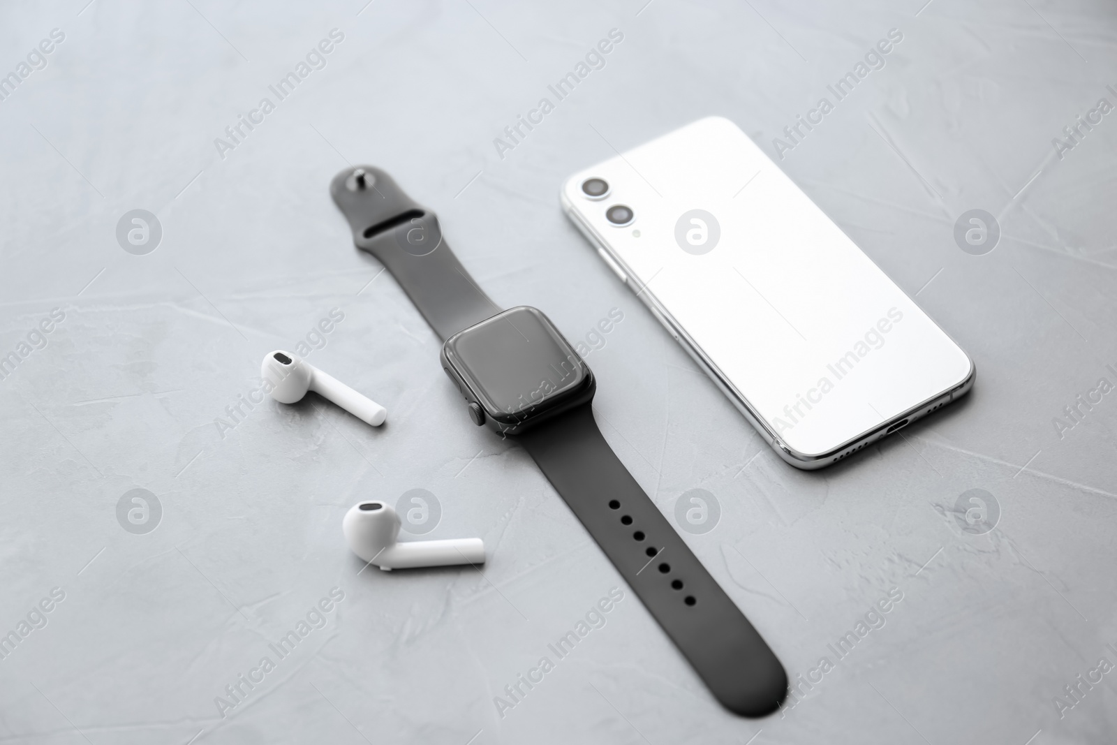 Stylish smart watch, phone and earphones on grey stone table Photo of Stylish smart watch, phone and earphones on grey stone table