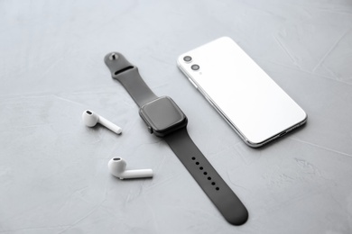 Photo of Stylish smart watch, phone and earphones on grey stone table
