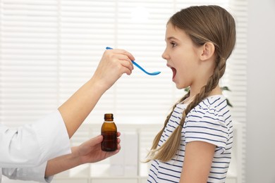 Doctor giving cough syrup to girl in clinic