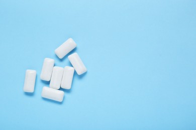 Photo of Tasty white chewing gums on light blue background, flat lay. Space for text
