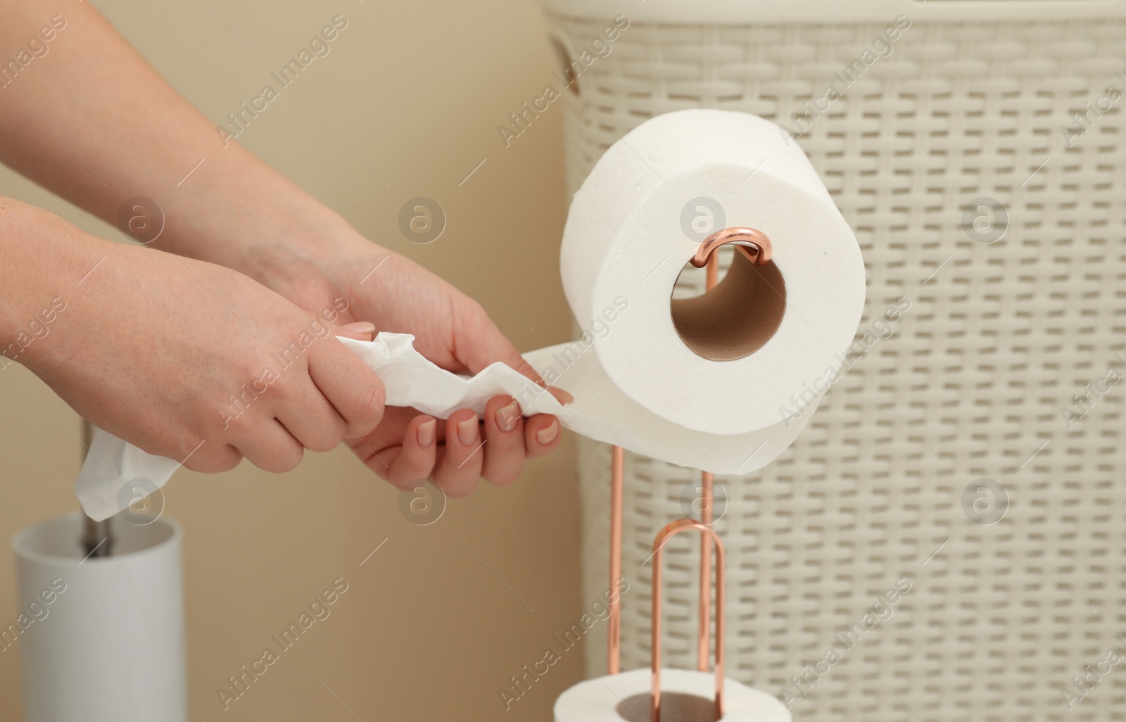 Photo of Woman taking toilet paper from roll holder in bathroom, closeup