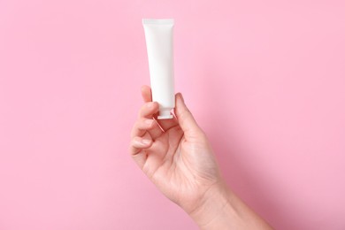 Photo of Woman with tube of hand cream on pink background, closeup