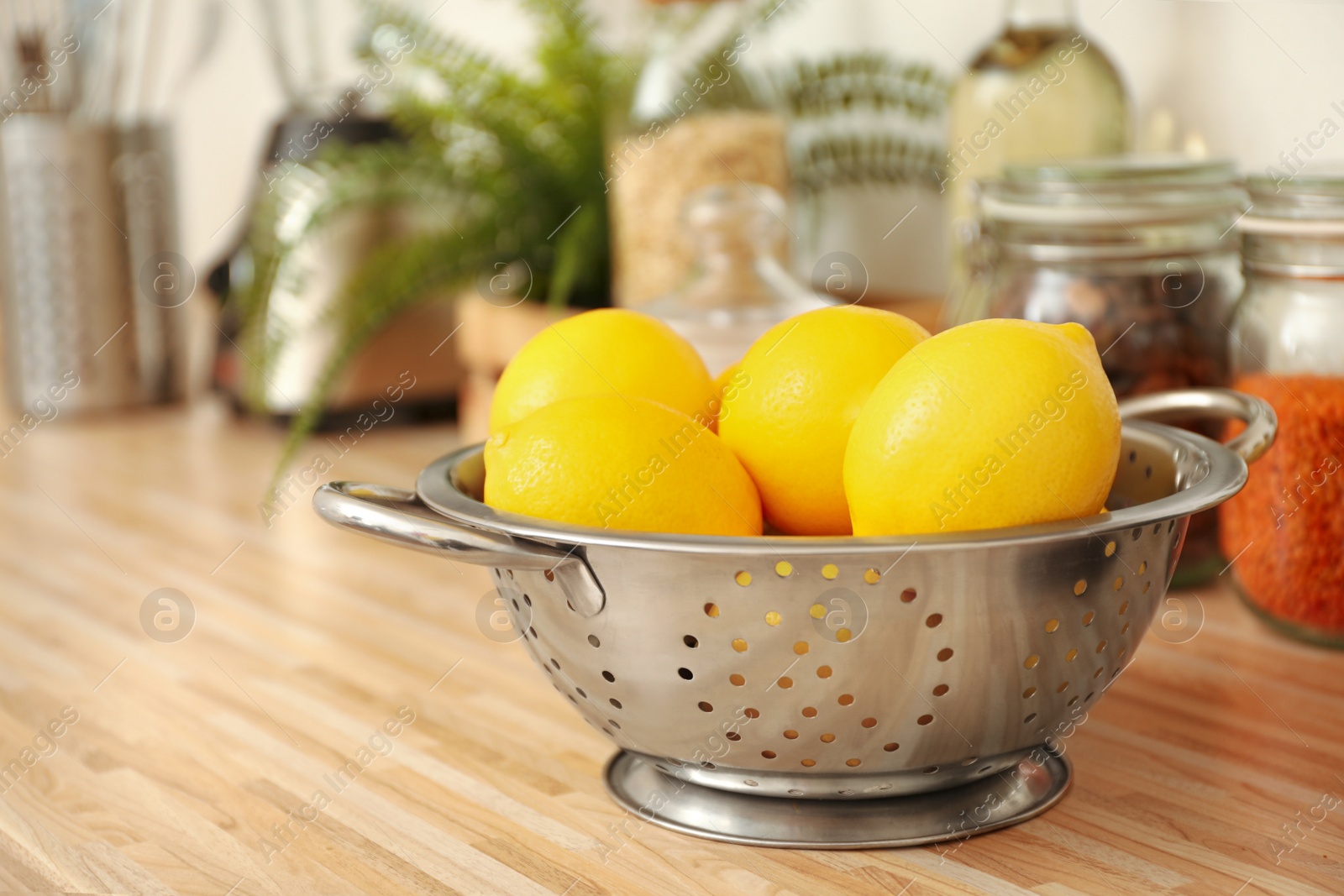 Photo of Fresh lemons in colander on wooden countertop. Kitchen interior element