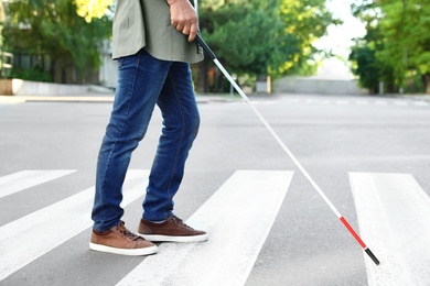 Photo of Blind person with white cane crossing street in city, closeup