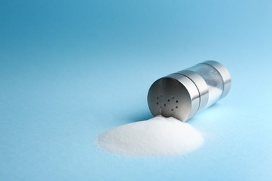 Photo of Scattered salt and shaker on light blue background, closeup. Space for text