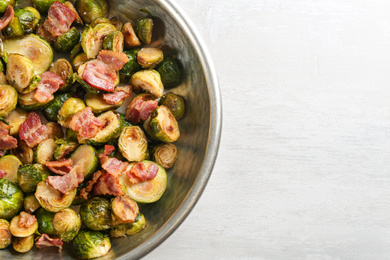 Roasted Brussels sprouts with bacon on white wooden table, top view. Space for text