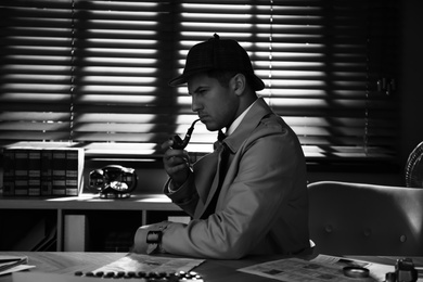 Old fashioned detective with smoking pipe at table in office. Black and white effect