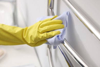 Photo of Woman cleaning heated towel rail with rag indoors, closeup