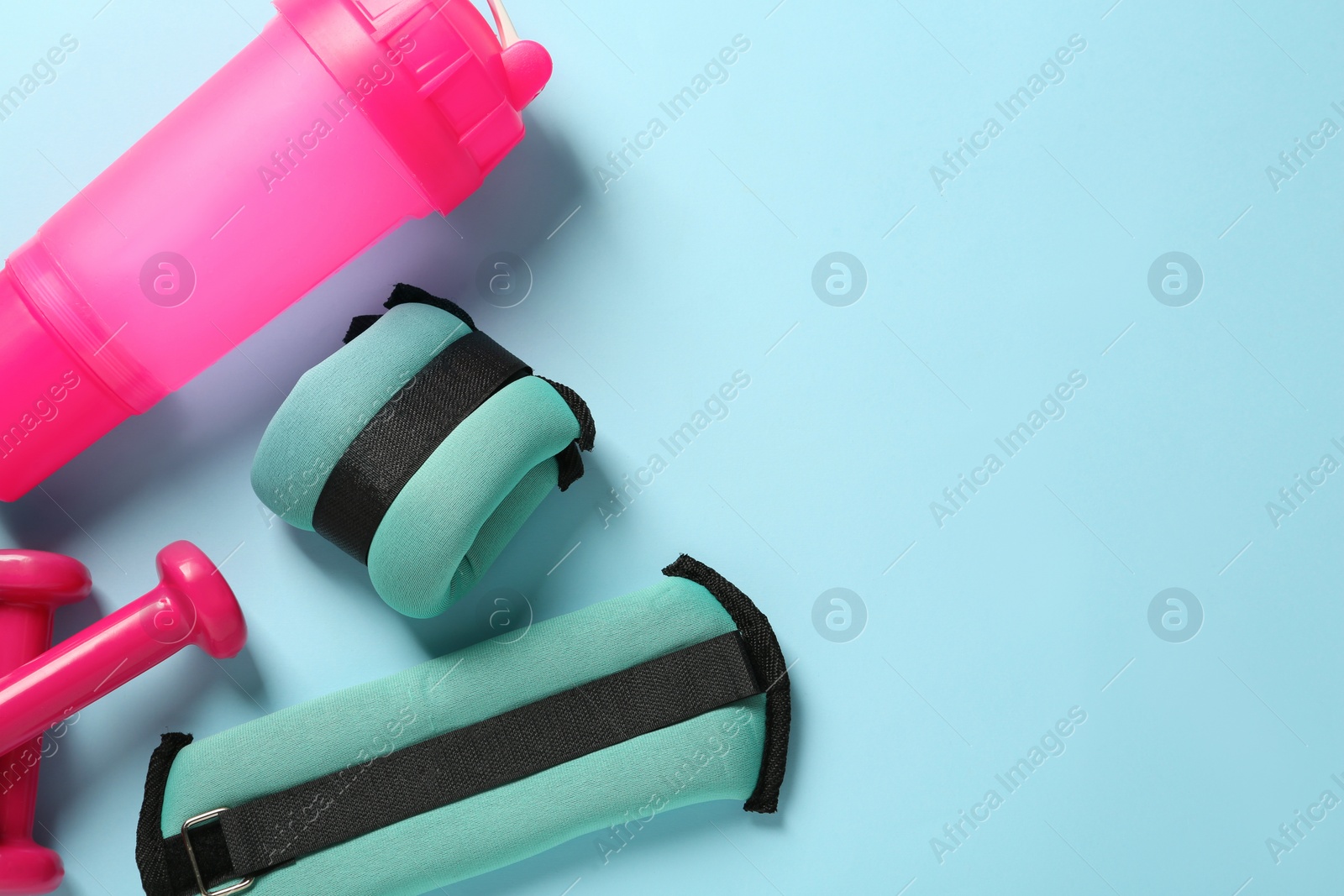 Photo of Turquoise weighting agents, dumbbells and shaker on light blue background, flat lay. Space for text