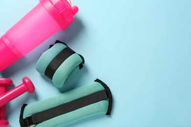 Photo of Turquoise weighting agents, dumbbells and shaker on light blue background, flat lay. Space for text