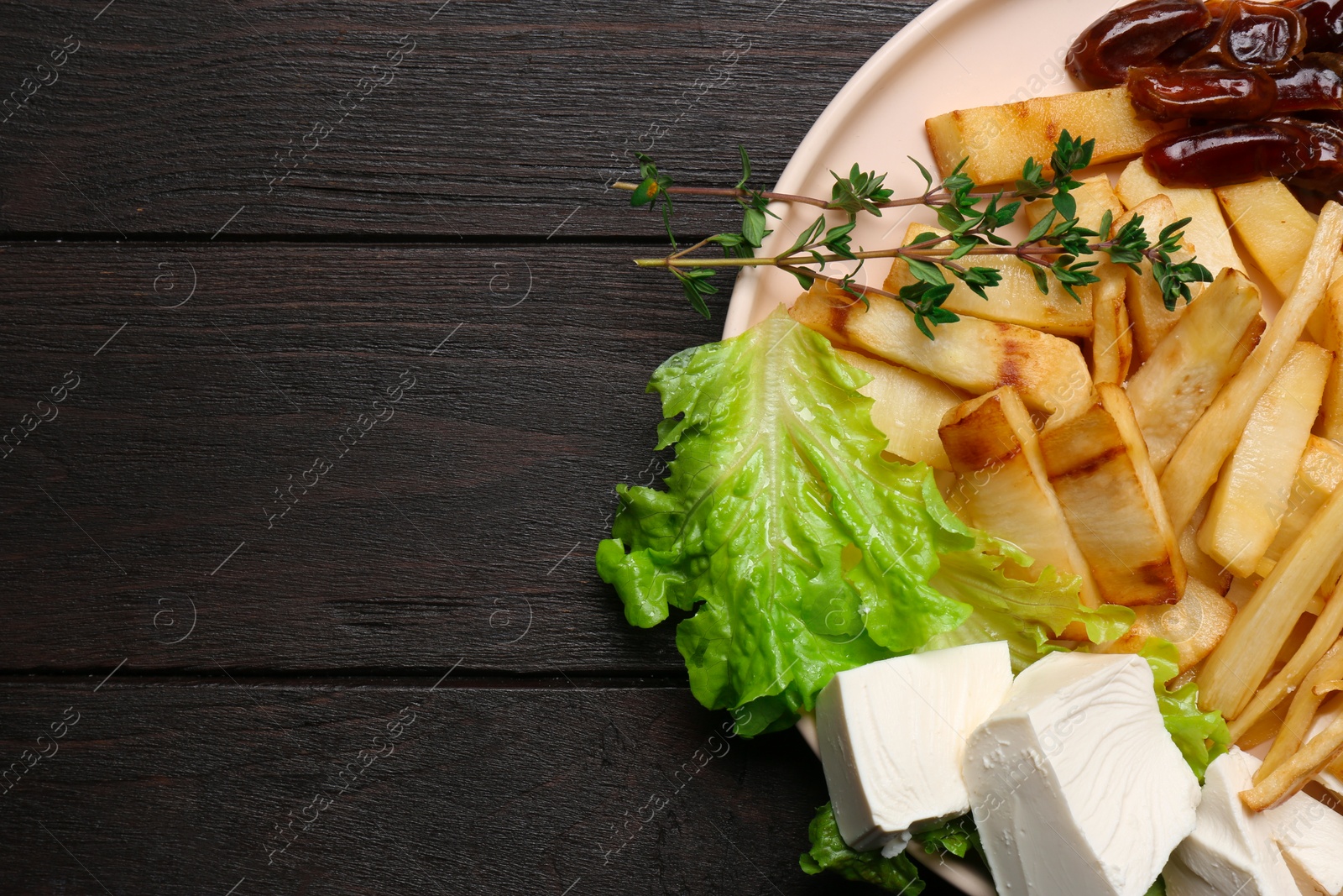 Photo of Delicious parsnip with lettuce, feta cheese and dates on black wooden table, top view. Space for text