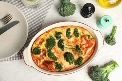 Tasty broccoli casserole in baking dish on white wooden table, flat lay