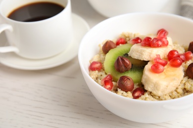 Photo of Bowl of quinoa porridge with hazelnuts, kiwi, banana and pomegranate seeds served for breakfast on white wooden table