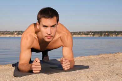 Photo of Sporty man doing plank exercise on beach
