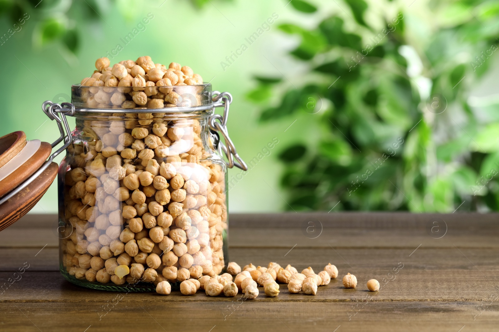 Photo of Raw chickpeas in jar on wooden table. Space for text