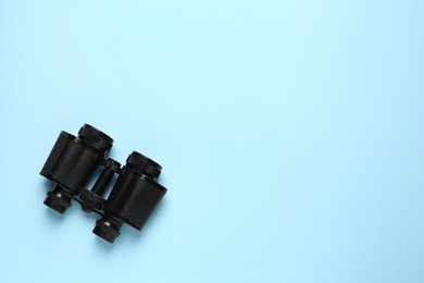 Photo of Modern binoculars on light blue background, top view. Space for text