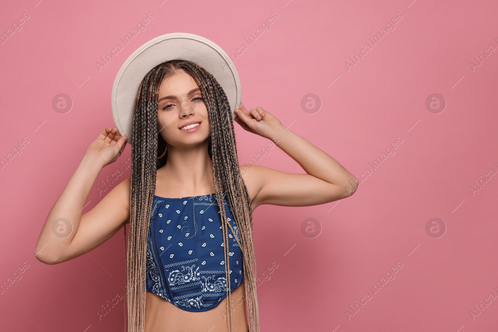Photo of Beautiful woman with long african braids and hat on pink background, space for text