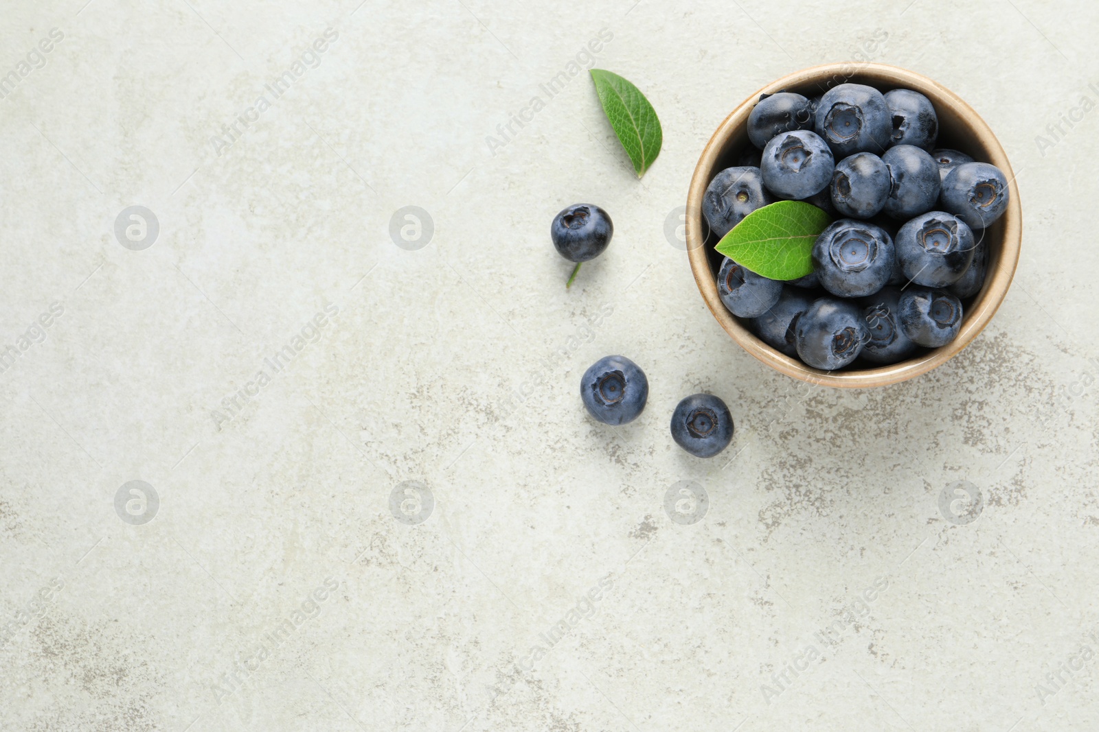 Photo of Tasty fresh blueberries in bowl on light table, flat lay. Space for text