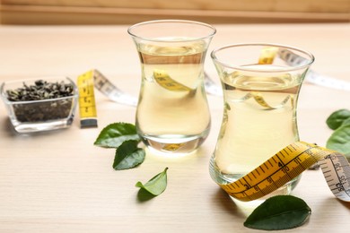 Photo of Diet herbal tea, measuring tape and green leaves on wooden table