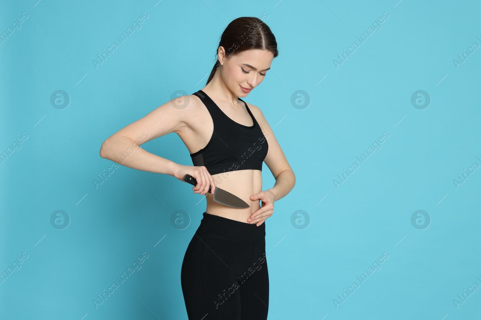 Photo of Slim young woman with knife on light blue background. Weight loss surgery