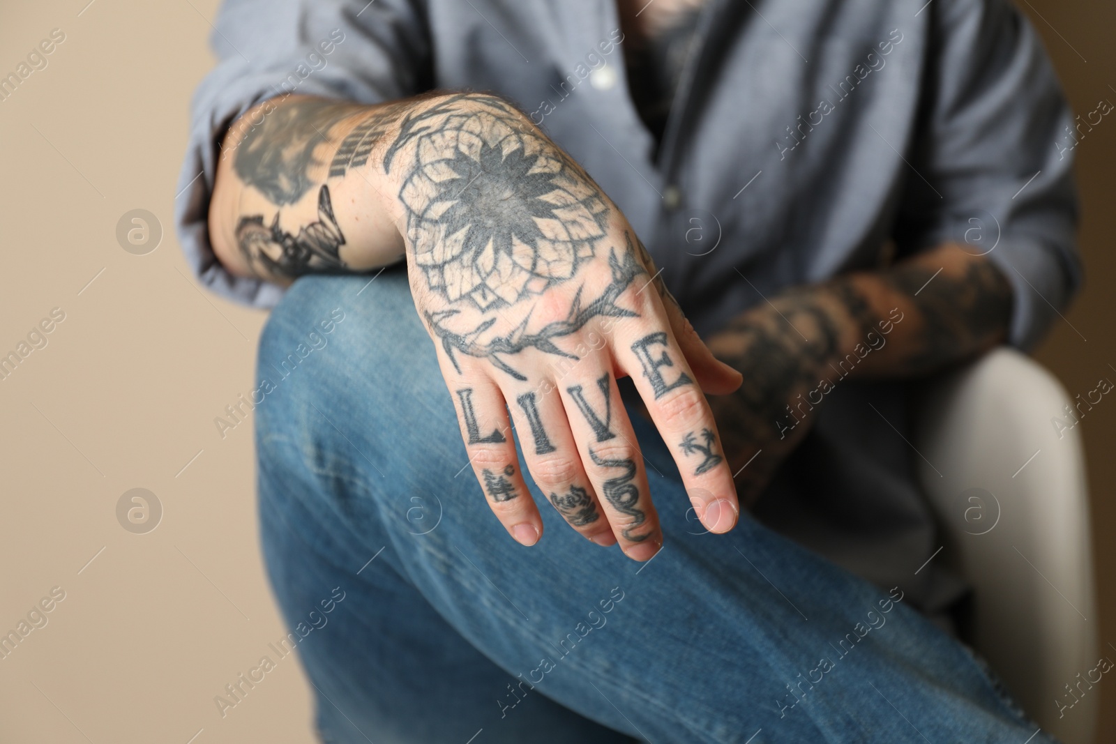 Photo of Young man with tattoos on arms against beige background, closeup