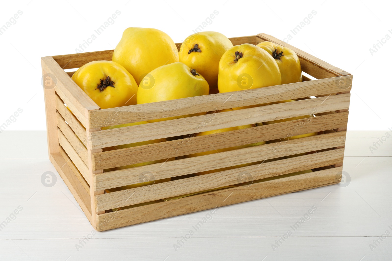 Photo of Crate with delicious fresh ripe quinces on light wooden table against white background