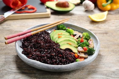 Photo of Plate of cooked brown rice with avocado and chopsticks on table