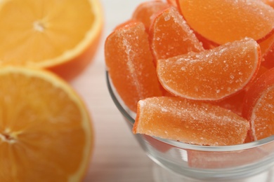 Photo of Tasty jelly candies in glass bowl and cut fruit on white table, closeup. Space for text