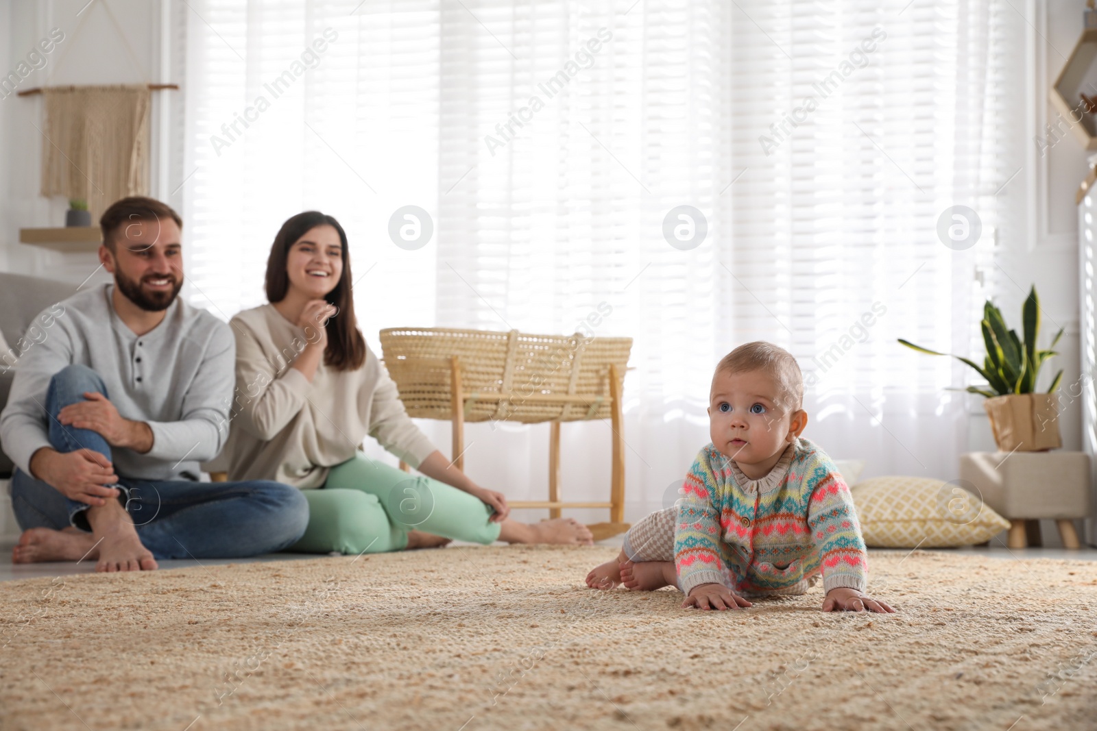 Photo of Happy parents watching their baby crawl on floor at home