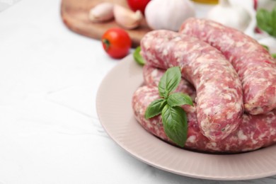 Photo of Raw homemade sausages and basil leaves on white table, closeup. Space for text