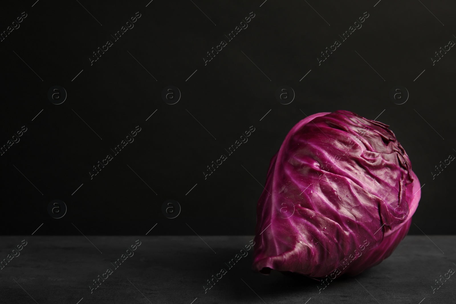 Photo of Pointed red cabbage on table against black background. Healthy food