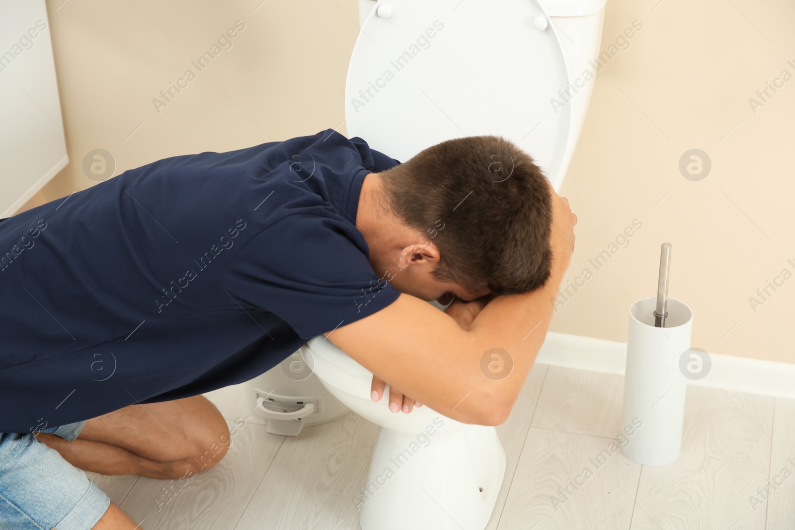 Photo of Young man vomiting in toilet bowl at home