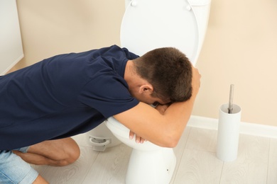 Young man vomiting in toilet bowl at home