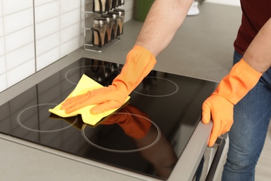 Young man cleaning oven cooktop with rag in kitchen, closeup