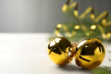 Photo of Golden sleigh bells on white table, closeup. Space for text