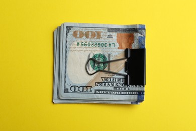 Photo of Dollar banknotes with paper clip on yellow background, top view