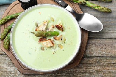 Bowl of delicious asparagus soup served on wooden table, flat lay