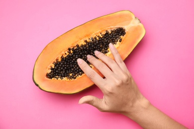 Photo of Young woman touching half of papaya on pink background, top view. Sex concept