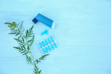 Photo of Ragweed (Ambrosia) branch, inhaler and pills on blue wooden table, flat lay with space for text. Seasonal allergy