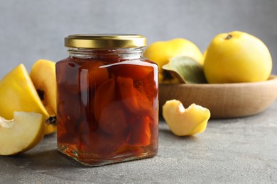 Tasty homemade quince jam in jar and fruits on grey textured table, closeup
