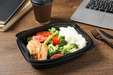 Photo of Container with tasty food, laptop, cutlery and cup of coffee on wooden table. Business lunch