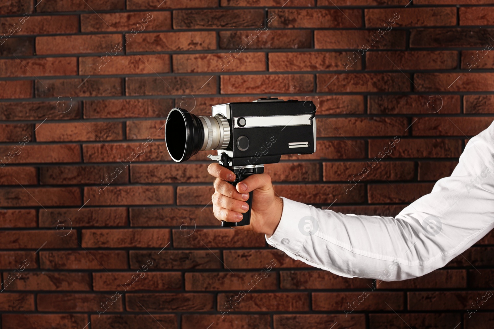 Photo of Man with vintage video camera near brick wall, closeup of hand