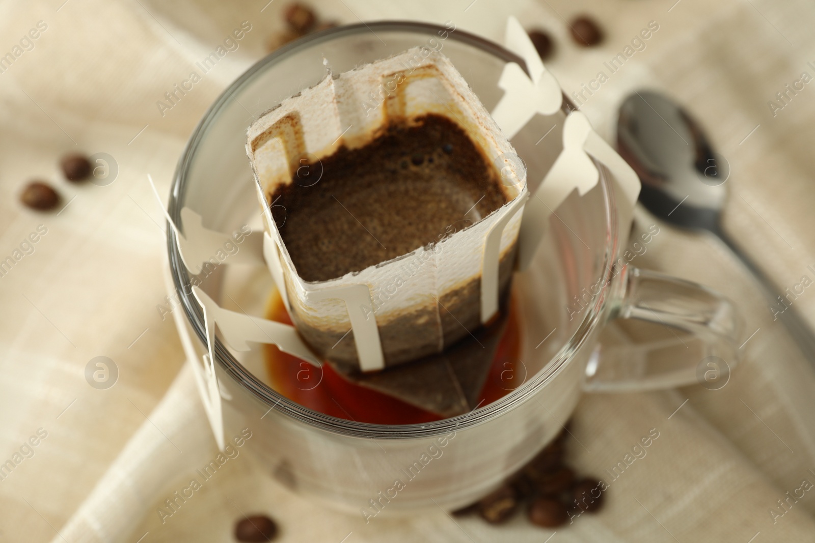 Photo of Glass cup with drip coffee bag on beige fabric, closeup
