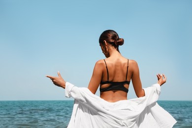 Young woman in stylish bikini near sea on sunny day, back view